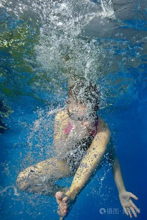 一个小女孩在游泳池里参加体育活动在水里泡着泡泡肖像在水下射击垂直