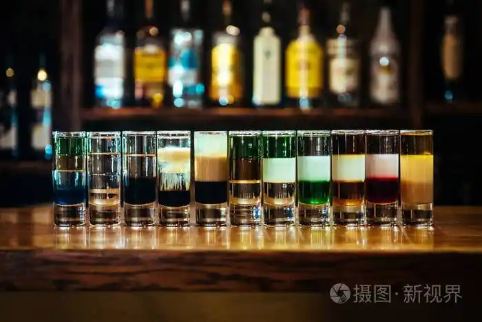 不同的酒精鸡尾酒酒瓶背景的酒吧里的木制桌子上的多层短饮料