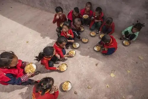孩子们没有餐桌,大一点的孩子一起在教室外面的操场上坐着吃饭,饭碗太