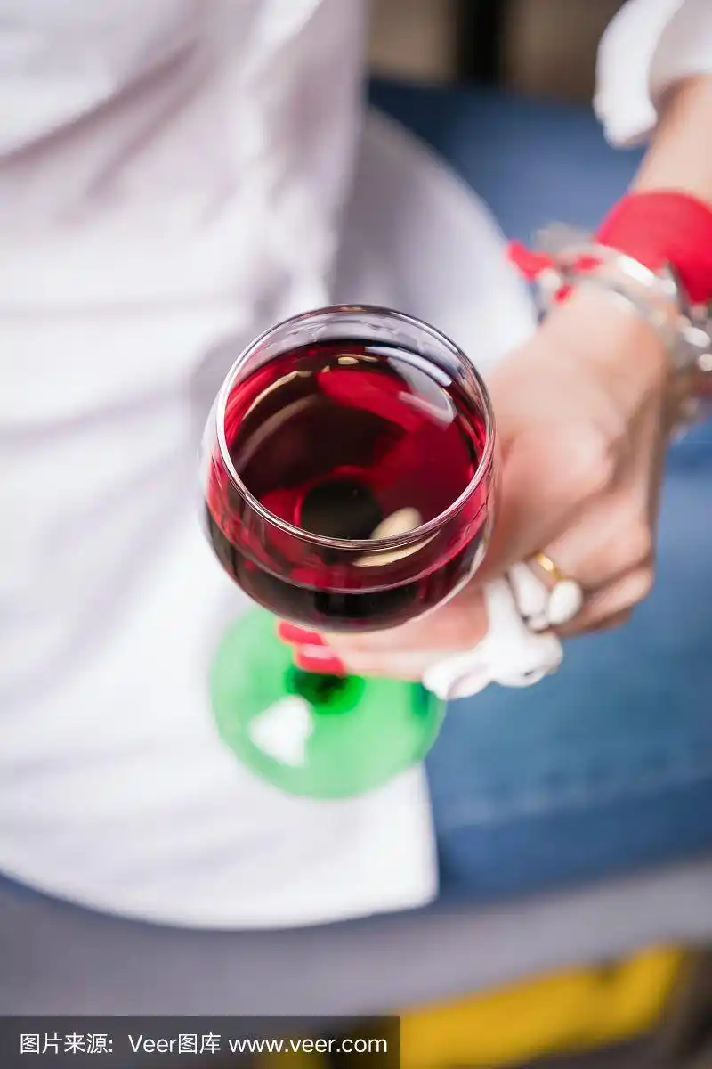 美丽的女性手握红酒杯在灯光背景