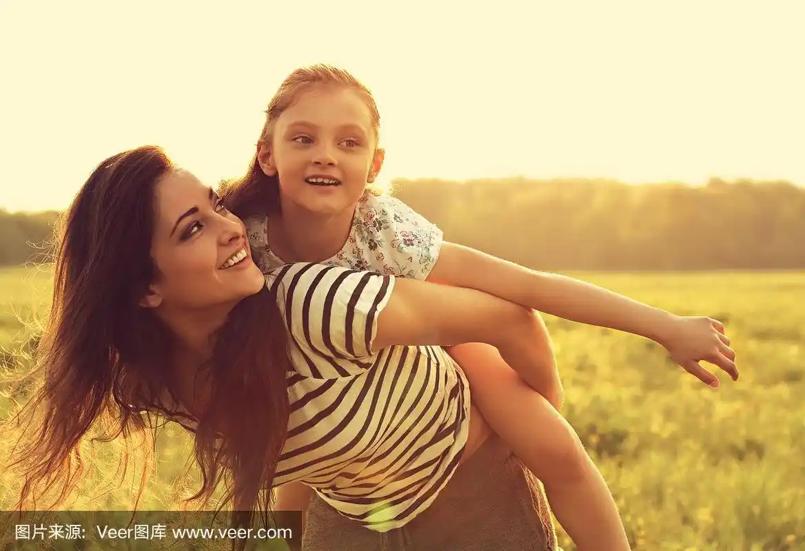 飞着的小女孩笑着快乐地享受着妈妈的背影,在夕阳明媚的夏日背景下.