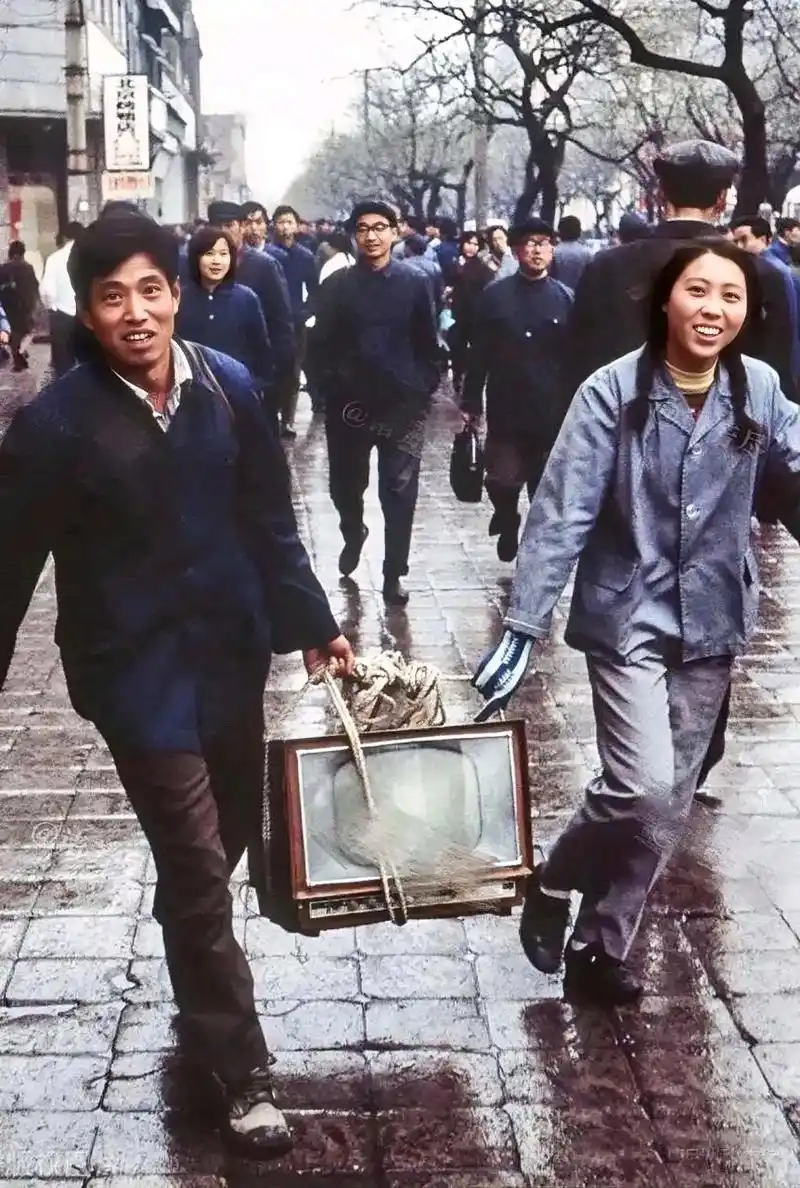 老照片:70年代,北京街头,一对夫妻抬着一台黑白电视机回家,高兴得合不