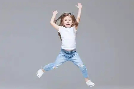 穿着蓝色牛仔裤白色t恤和太阳镜的学龄前儿童在灰色背景下孤立地举起