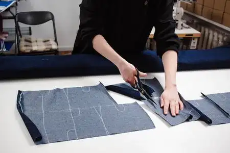 女裁缝用白色桌上的剪刀剪牛仔裤面料的手照片