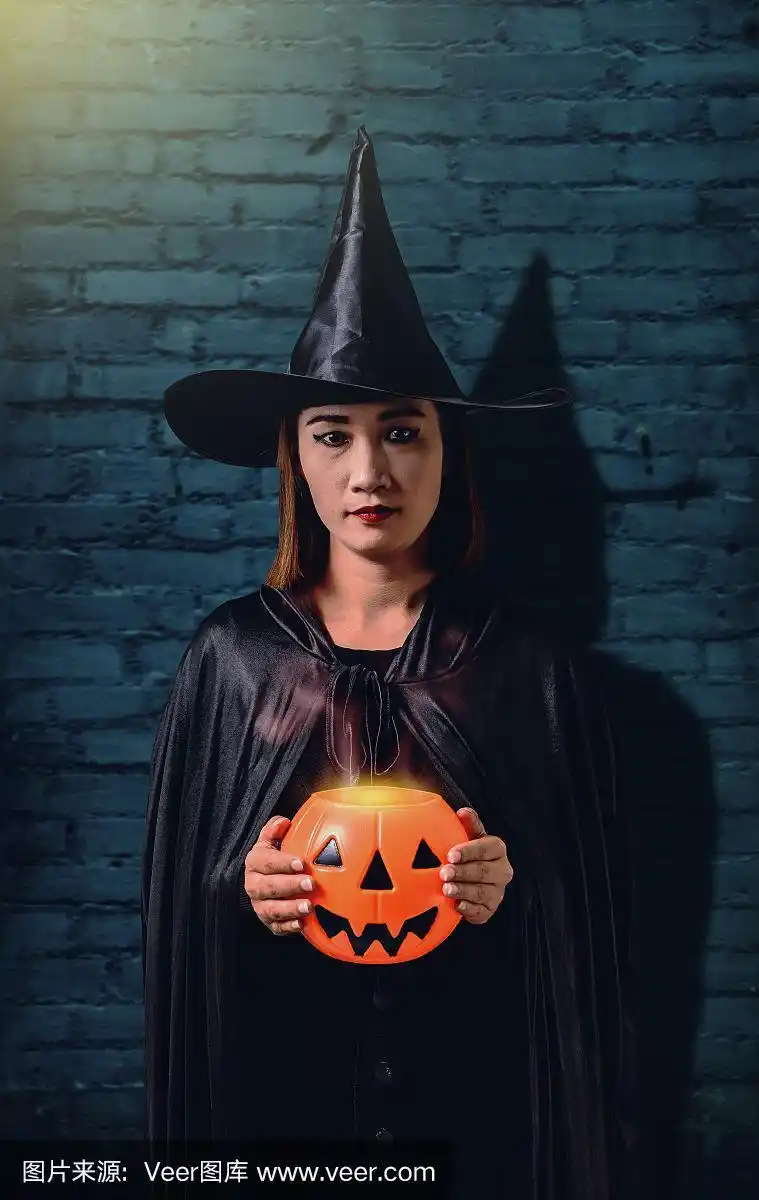 女人在黑色可怕的巫婆万圣节服装与老砖墙的古老城堡的女巫