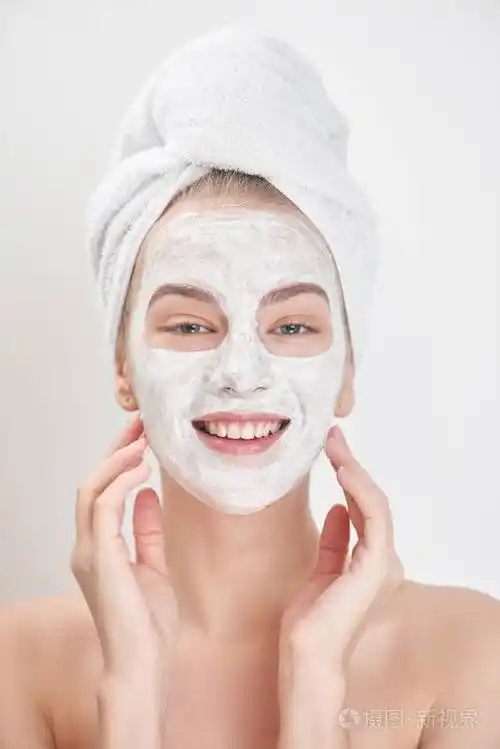 戴着毛巾的微笑的女人脸上涂抹口罩美容治疗理念