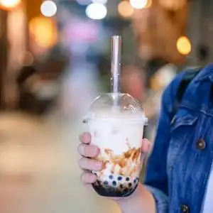 喝红糖在台湾夜市,年轻女子拿着,喝着红糖味的木薯珍珠泡奶茶照片