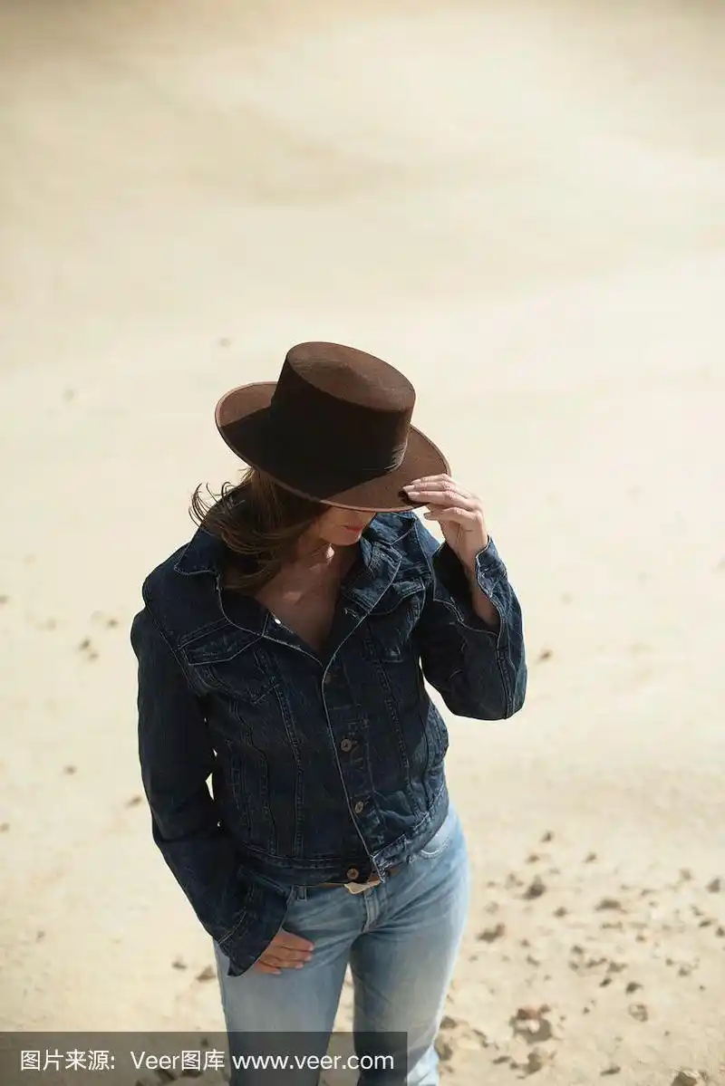 棕色帽子和牛仔裤夹克的黑发女人站在沙漠里.