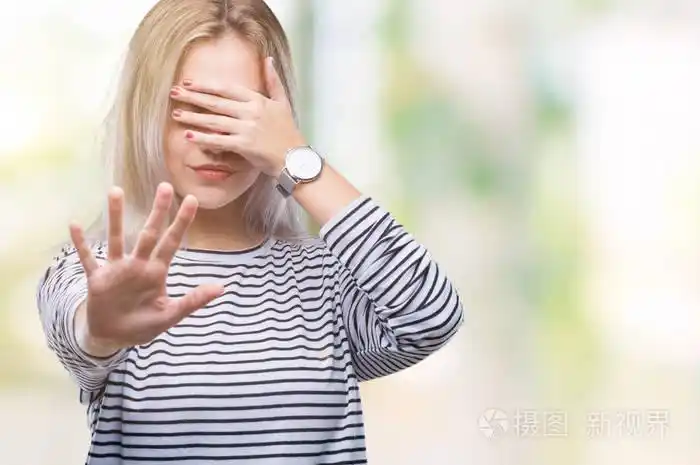 年轻的金发女人在孤立的背景上用手遮住眼睛,用悲伤和恐惧的表情做