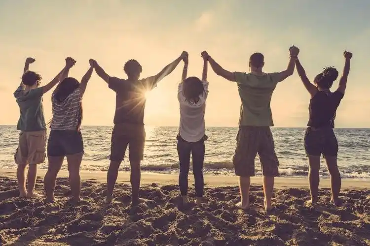 夕阳背景中海边举起手臂的一群年轻人