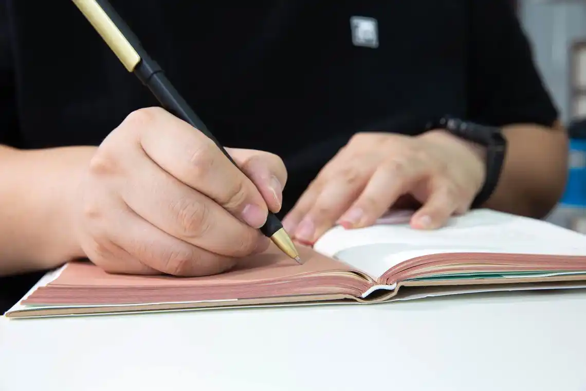 特写亚洲青年男子的学生拿着笔在书本上写字