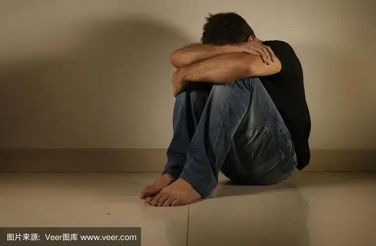 年轻绝望和抑郁的男人独自哭泣坐在家里地板在阴暗和