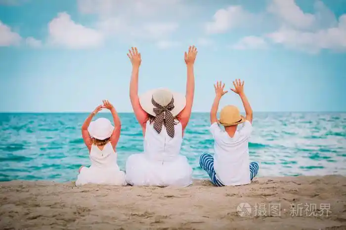 快乐的妈妈带着两个孩子在沙滩上举手