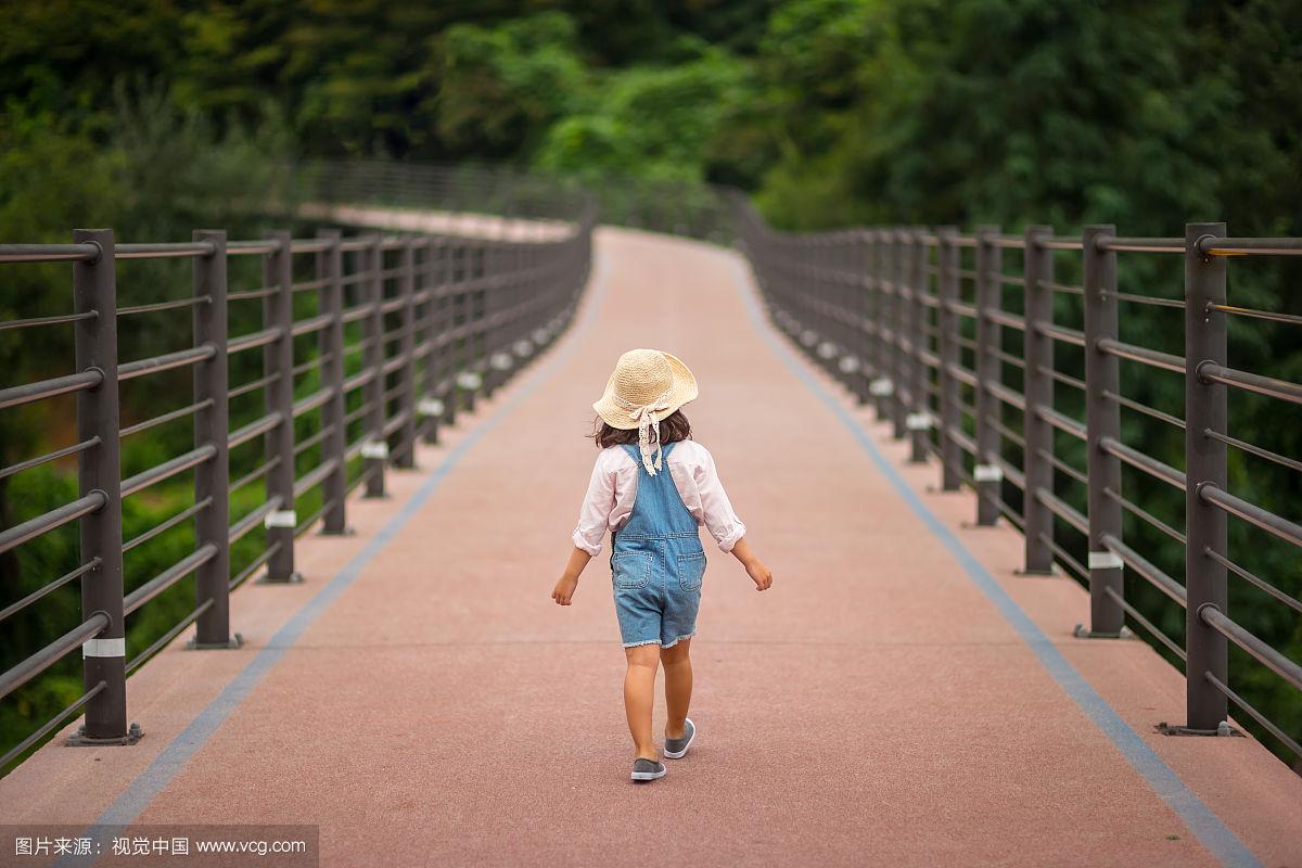戴着帽子的小女孩在公园的街道上行走的背影
