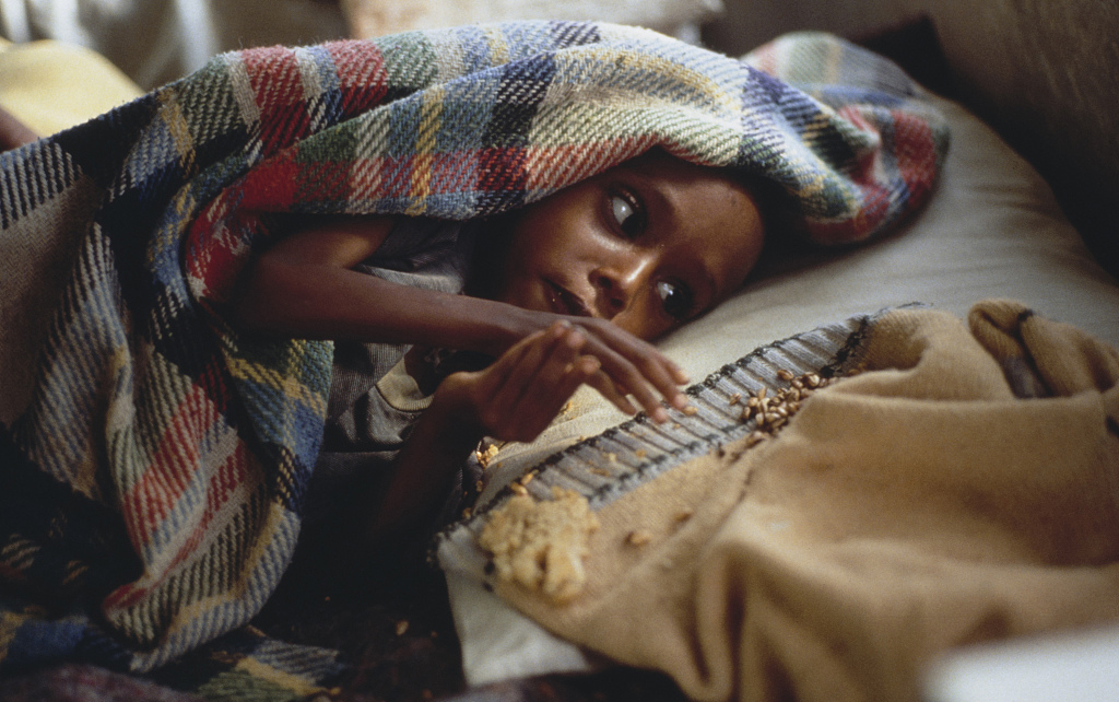 埃塞俄比亚提格雷地区的难民中心,一个孩子伸手去拿毯子上的食物.