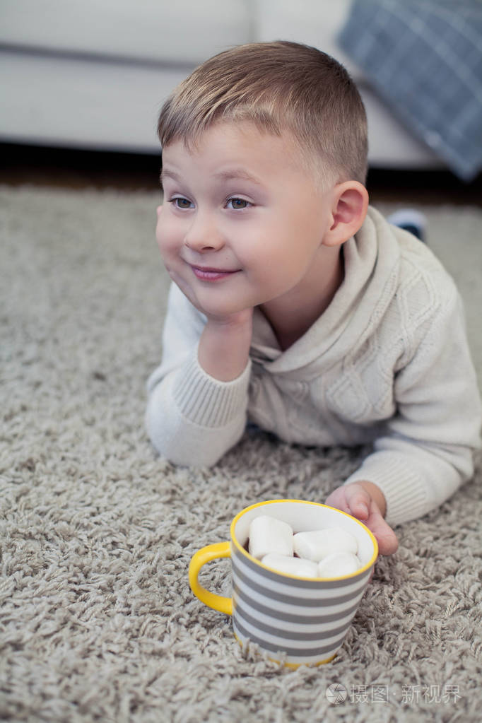 一个4岁的小男孩坐在地毯上喝可可.秋天