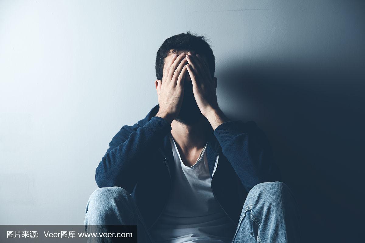 一个悲伤的男人坐在黑暗背景的地上