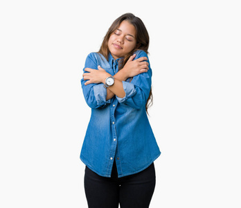 年轻漂亮的黑发女人穿着蓝色牛仔衬衫,在孤立的背景下拥抱自己,快乐而