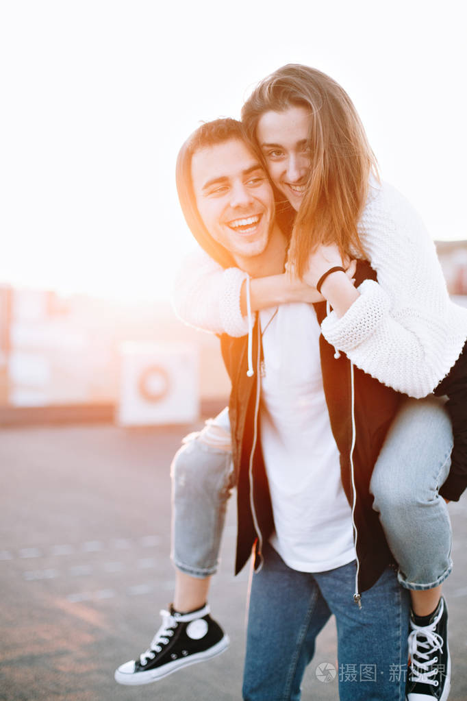 年轻夫妇在爱傻瓜周围和有乐趣在屋顶在日落, 笑和