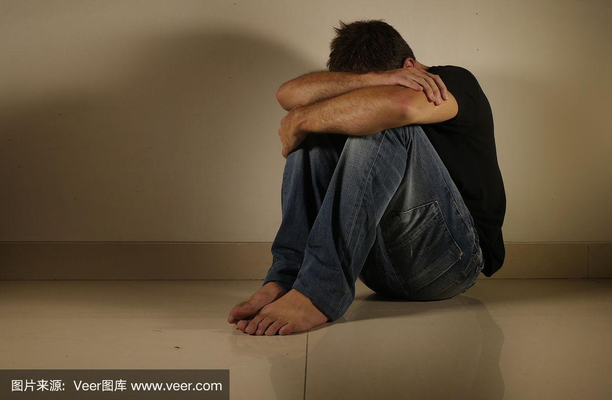 年轻绝望和抑郁的男人独自哭泣坐在家里地板在阴暗和