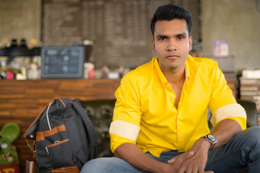 年轻英俊的印度男人坐在咖啡店坐在咖啡店的年轻英俊的印度男人的肖像