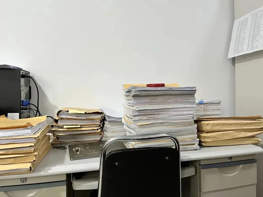 在不到10平米的房间里,每张桌子上都堆满了一摞一摞的卷宗,让5个人的